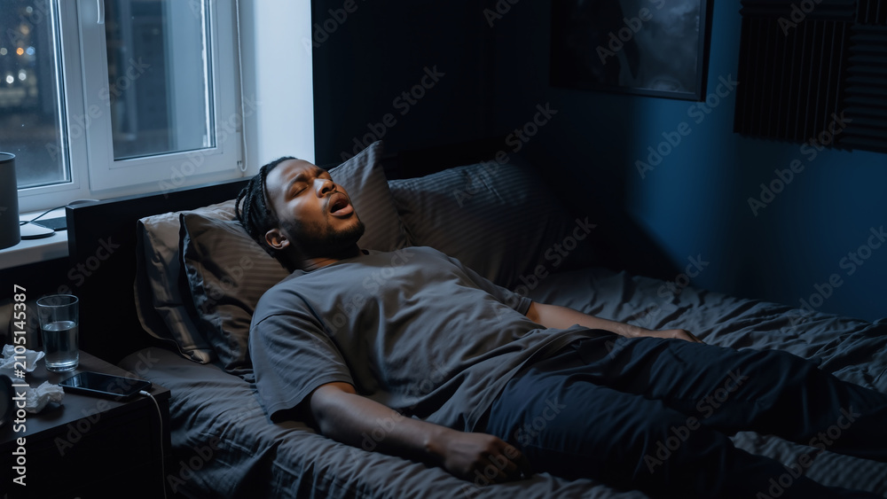Fototapeta premium Black man patient lying on bed gasping for air in dark bedroom at night. Sleep apnea and sleep disorder awareness