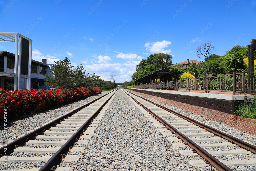 Obraz premium Vintage Train Station Platform and Railway Tracks Under Clear Blue Sky