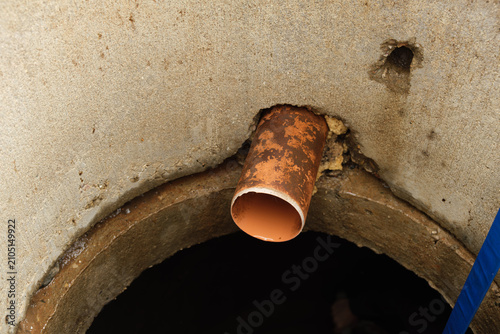 An orange plastic pipe protrudes from a concrete ring into overflow sewer well. Drainage system. A service cleaning of blocked sewer. Maintenance work, utility service, underground infrastructure.