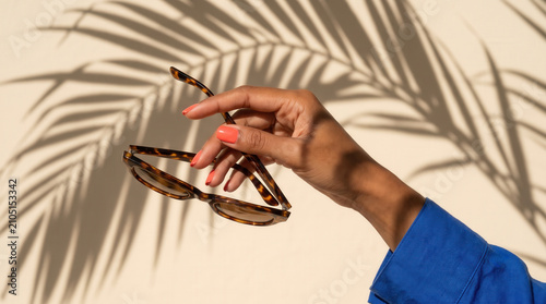 Woman Holding Tortoiseshell Sunglasses Against Palm Leaf Shadows