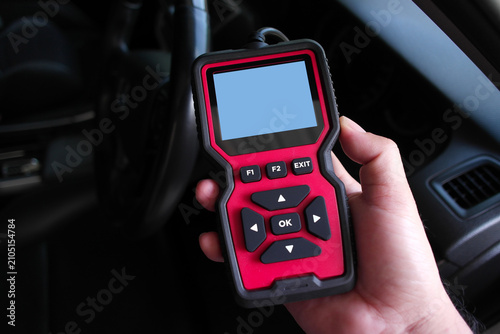 A hand holding a OBD2 code reader with blank screen inside a car cabin, ready to diagnose vehicle errors, check engine issues, and perform auto maintenance