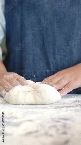 Vertical video: Floured hands shaping dough ball after resting at bench for proofing, denim apron