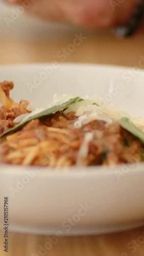 Vertical video: Hand entering twirling fork in bowl on wood table, lifting noodles toward mouth