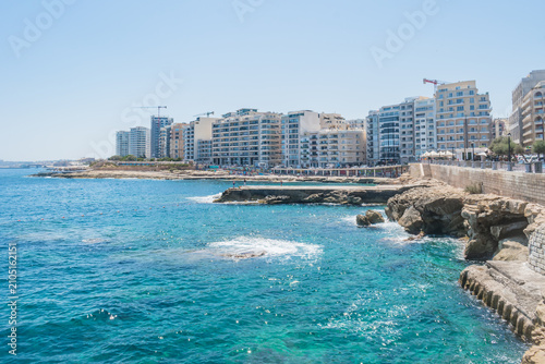 Turquoise sea landscape at Qui-Si-Sana Beach with buildings in the background, Sliema MALTA