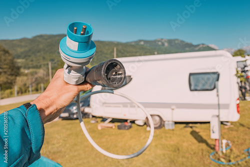 Tablou pe pânză Hand holding electric hookup adapter cable at caravan campsite with mountains