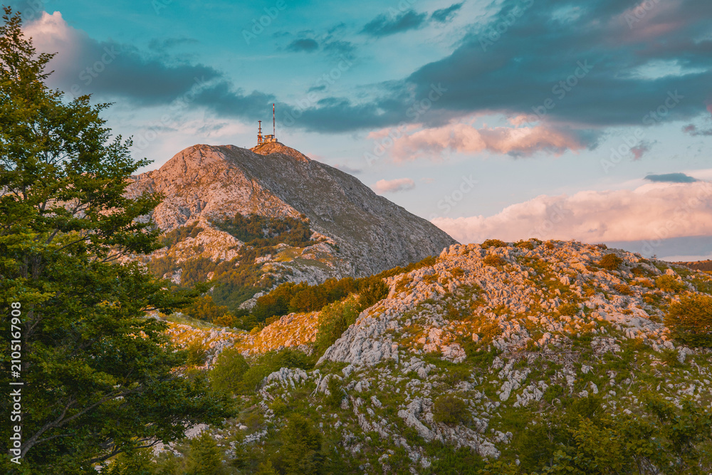 Naklejka premium Rocky Lovcen mountain landscape with communication antennas on peak, illuminated by warm evening sun in Montenegro