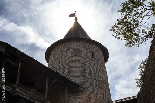 Fotografía Historic medieval stone fortress watchtower with a wooden conical roof and weather vane, backlit by the bright sun in a blue cloudy sky