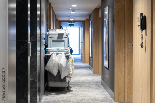 A housekeeping cart stands inside a modern hotel corridor during daily cleaning service, highlighting essential maintenance operations within a professional hospitality facility