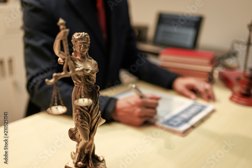 Foto Lady justice statue in foreground with a lawyer writing at a desk in an office,