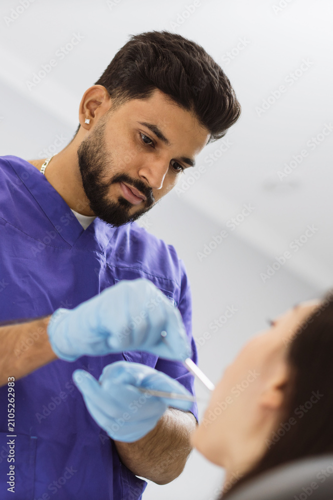 Fototapeta premium A male dentist in blue scrubs and gloves performs a dental examination on a patient with specialized tools