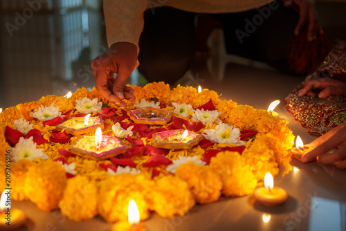 Canvastavla Cropped hands arranging burning clay diyas on floral marigold rangoli for Diwali