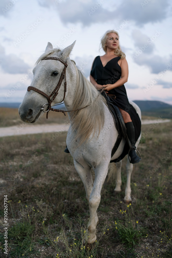 Fototapeta premium Woman horse riding elegant blonde across a grassy plain under a dramatic cloudy sky