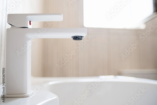Close-up view of a modern white bathroom water faucet with limescale buildup on the aerator spout in a bright room.