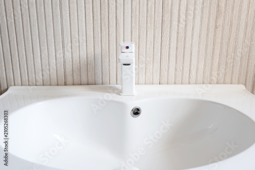Front view of a clean modern white ceramic bathroom sink basin and mixer faucet against a wood panel wall.