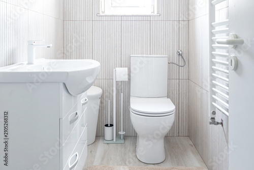 Wide view of a modern bright white bathroom interior featuring a sink vanity unit, ceramic toilet, and tiled walls.