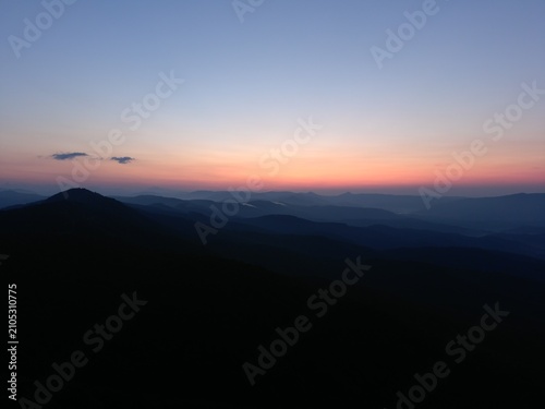 Beautiful aerial drone view of layered mountain ranges at sunrise with soft morning mist, colorful sky and peaceful wilderness. Natural landscape background ideal for travel, tourism, adventure, outdo