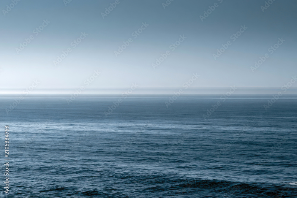 Fototapeta premium The soft blue hues of a misty ocean horizon create a tranquil and dreamy atmosphere, inviting viewers to reflect on the vastness and beauty of the sea at dawn.
