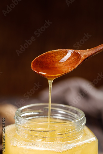 Foto Raw Wild Honey with Crystallized Texture Dripping from Wooden Spoon into Glass J