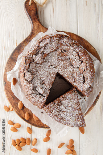 Torta Caprese Italian Flourless chocolate Cake closeup on the wooden board on the table. Vertical top view from above
