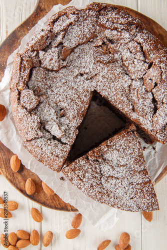 Italian torta caprese: this chocolate and almond cake is dense, rich and moist closeup on the wooden board on the table. Vertical top view from above