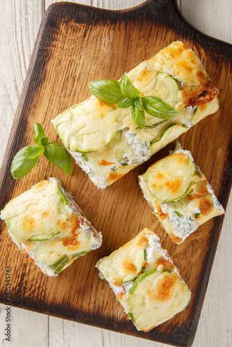 delicious roll of baked zucchini with cheese, stuffed with salmon and cream cheese, close-up on a wooden board on the table. Vertical top view from above