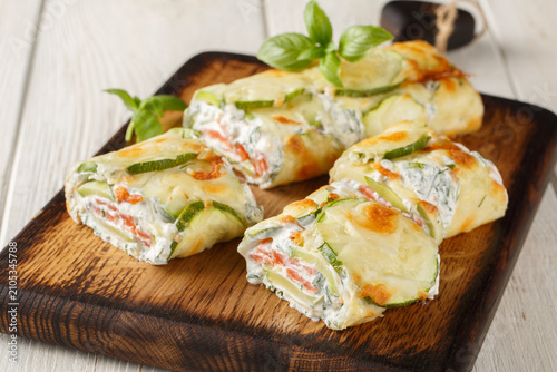 Appetizer Roll of sliced ​​zucchini stuffed with salmon and cream cheese close-up on a wooden board on the table. Horizontal
