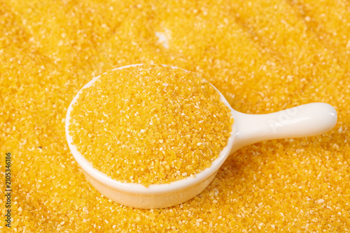 Fotografie Yellow corn grits polenta in wooden spoon on golden background - healthy cooking