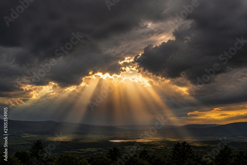 Schilderij op canvas Dramatic sunbeams breaking through dark storm clouds over a landscape, cinematic lighting