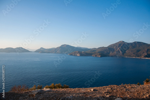 Beautiful panoramic viewpoint overlooking a calm blue sea bay surrounded by mountains and cliffs under a clear evening sky in Fethiye, Turkey