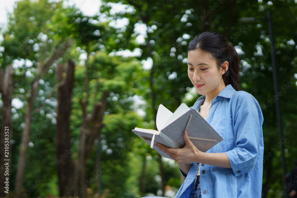 Fototapeta premium Education, university and woman in campus, Young asian woman smiles widely while tacking note. She standing in campus with her ready. Enjoying education outdoors with textbook