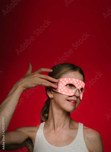 Red light therapy eye mask. smiling woman profile wearing infrared light therapy mask. touching the mask with her fit hand. dark background