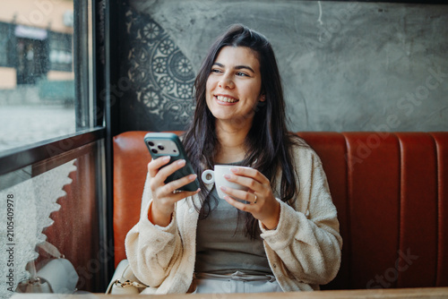 Woman smiling using phone drinking coffee in cafe