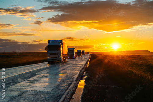 A truck is driving down the highway during an orange sunset, with the sun's rays