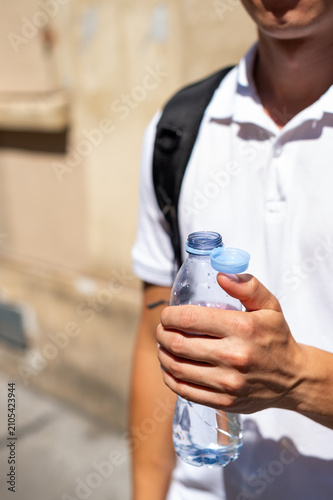 A person holds an open clear plastic water bottle with an attached tethered cap. The close-up shot focuses on sustainable packaging design for environmental conservation.