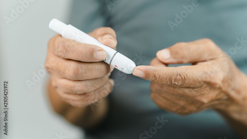 Fotografie Close-up of a senior adult using a lancet device for finger prick blood glucose monitoring at home
