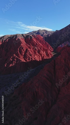 Drone vertical video flight above red canyon ridges and shadowed valley at Quebrada de las Señoritas in Jujuy, Argentina