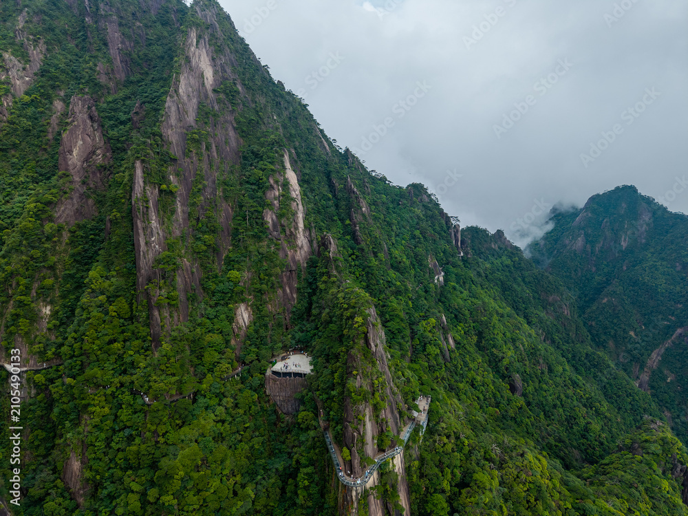 Obraz premium A high angle view showing the lush green peaks and winding cliff side walking paths of Sanqingshan Mountain located in Jiangxi province of China on a cloudy day