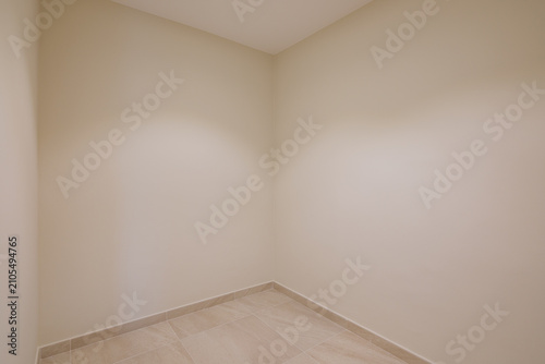 Empty beige interior room with tiled floor, soft natural light, clean neutral walls, unfurnished layout, minimalist style, calm residential space for modern property use