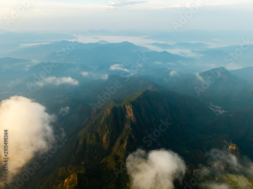 An aerial view captures the majestic peaks of Sanqingshan Mountain in Jiangxi China as thick white clouds drift through the deep green valleys during a beautiful morning