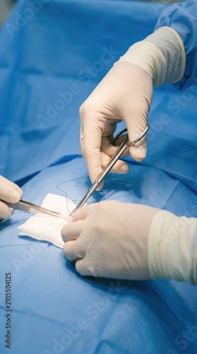 Surgeon performing skin suture on patient in operating room. Closeup of medical hands using needle holder and forceps during plastic surgery procedure. Healthcare and clinic operation.