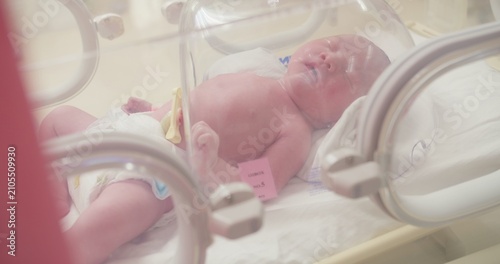 Fotografija A newborn infant with an umbilical cord clamp rests safely inside a modern hospital incubator, representing neonatal care and the fragility of new life