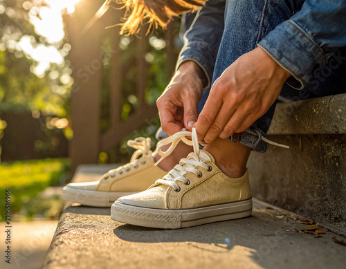 Person tying laces on casual sneakers outdoors in sunlight.