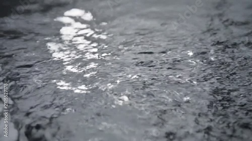 Close-up of water splash with light reflection. High-speed liquid droplet impact on surface creating dynamic ripples.