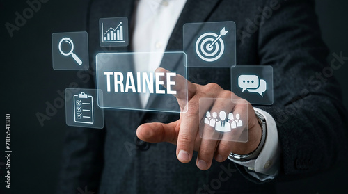 Training and Development Interface: A businessman's finger presses a glowing touchscreen, highlighting the word TRAINEE amidst a collection of digital icons representing business growth, targets.