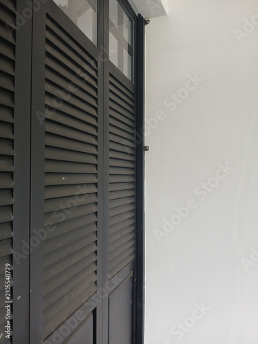 Dark black louvered shutters stand vertically against a clean minimalist white wall in this high angle architectural photograph capturing simple geometric lines and modern interior design elements for