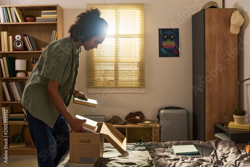 Teenager packing books into storage box in bedroom  preparing relocation or dorm move. Image supporting moving services  student housing  life transition  decluttering campaigns