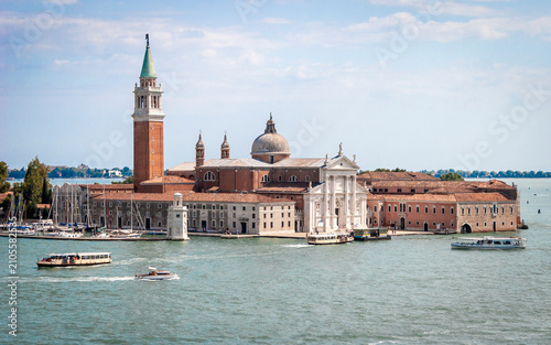San Giorgio Maggiore Venice. View across lagoon toward church bell tower and boats on sunny day.