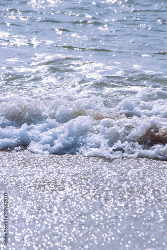 Fotografie Sunlit Waves Washing Ashore on a Sandy Beach