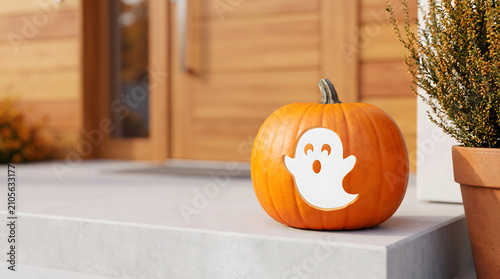 Pumpkin with ghost face sticker placed on front porch steps near wooden door