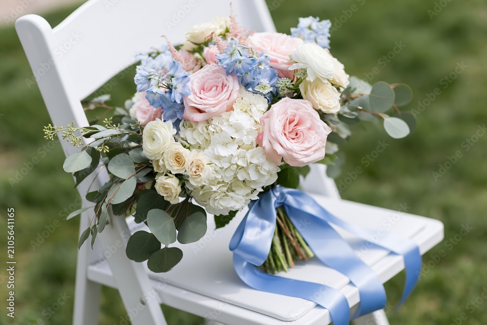 Fototapeta premium The pastel bouquet resting on a white chair with blue satin ribbon